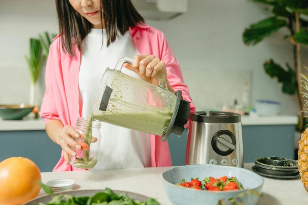 Woman making nutritious green smoothie in kitchen with fruits and vegetables.